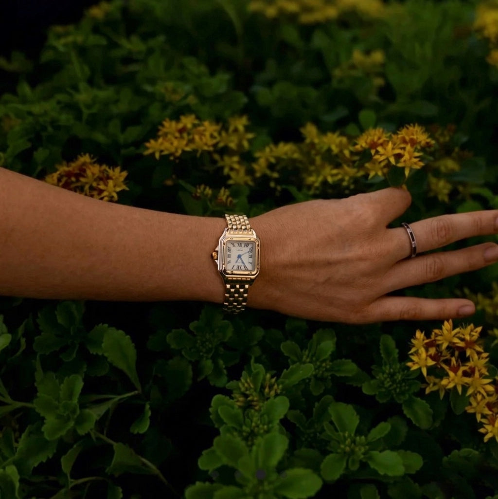 Woman wearing the gold Lumiere watch posing amidst green leaves and flowers