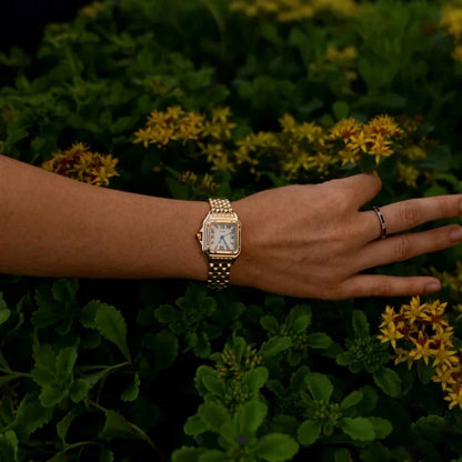 Woman wearing the gold Lumiere watch posing amidst green leaves and flowers
